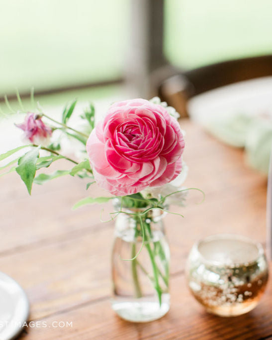 Table setting with pink flowers in a vase and a table number on a wooden table.