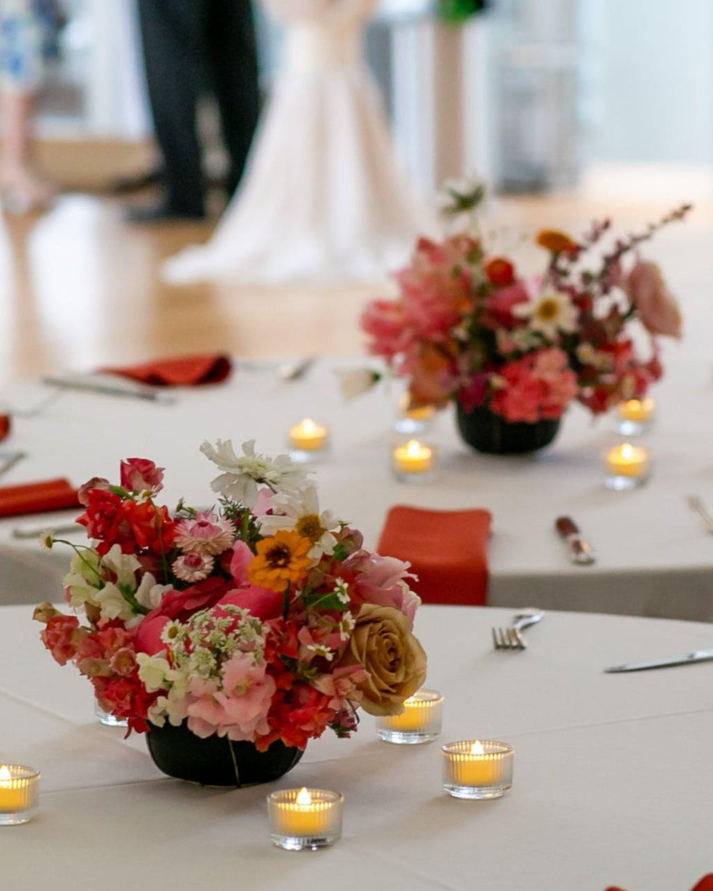 Decorated tables with red napkins, floral centerpieces, and candles in a formal setting.