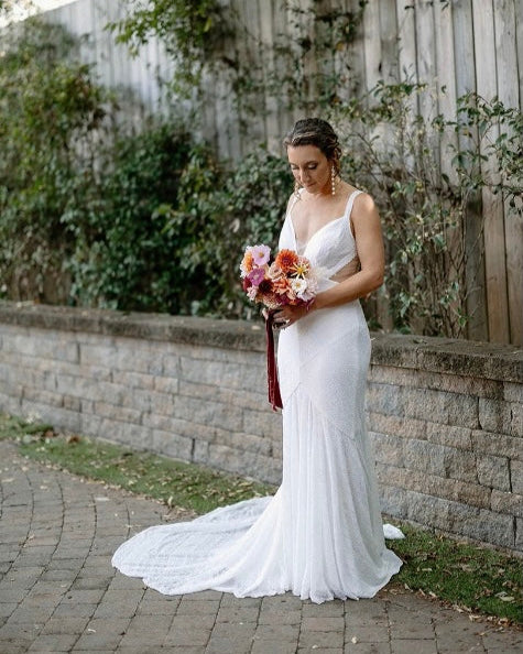 Woman in a white wedding dress holding a bouquet in an outdoor setting.