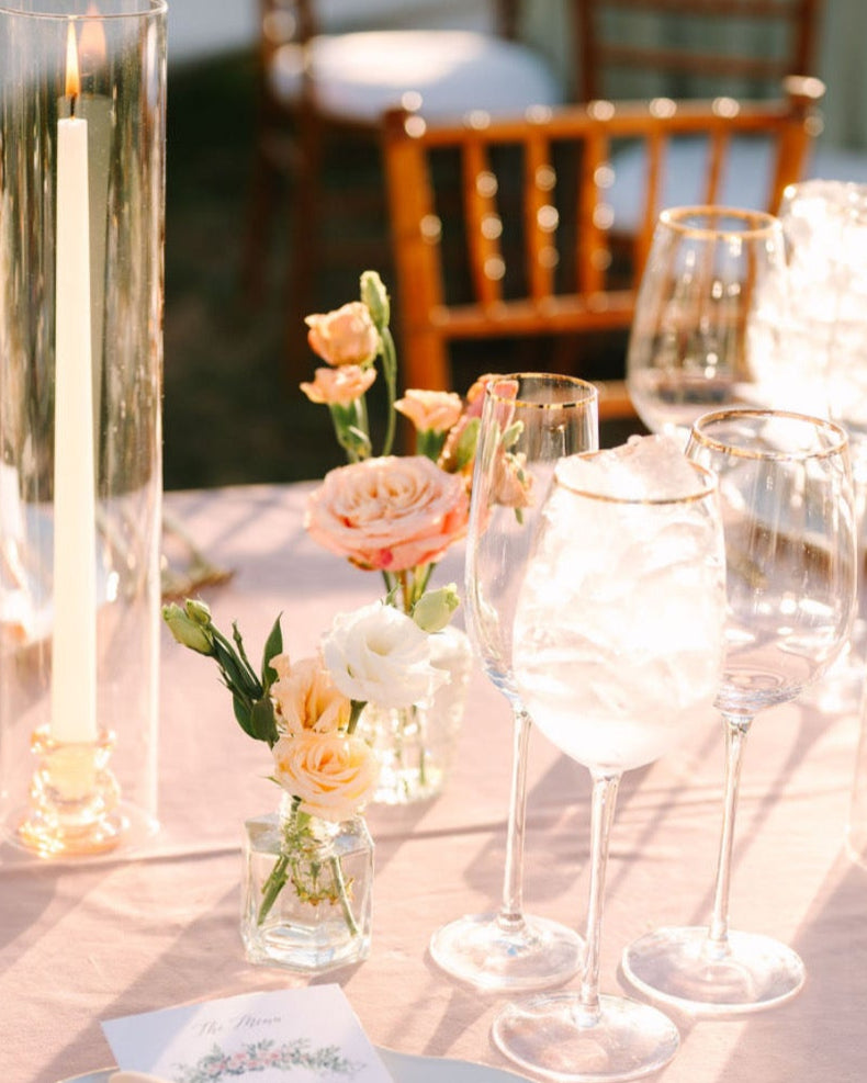 Elegant table setting with bud vases of flowers, candles, and cutlery on a tablecloth.