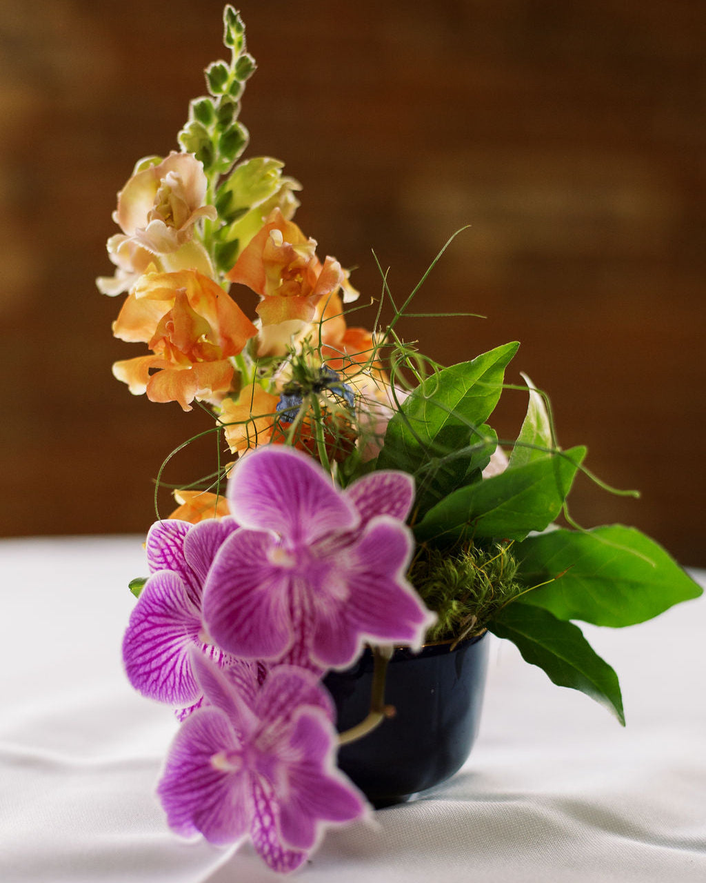 Floral arrangement with purple orchids and orange flowers on a white surface.