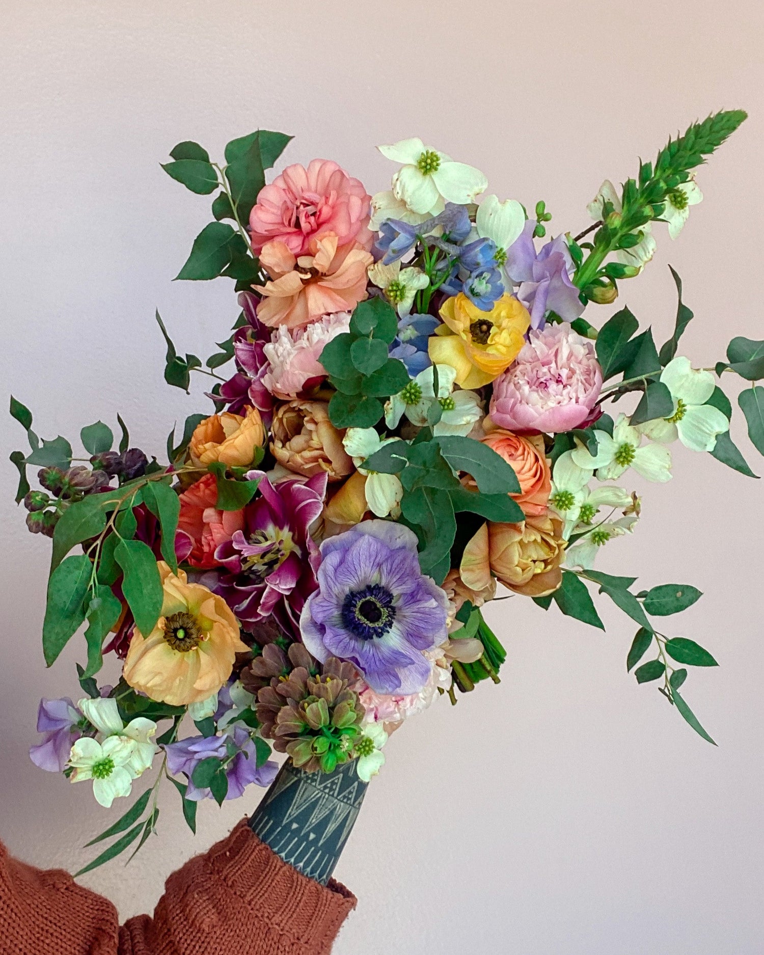 Bouquet of colorful flowers held by a person wearing a brown sweater.
