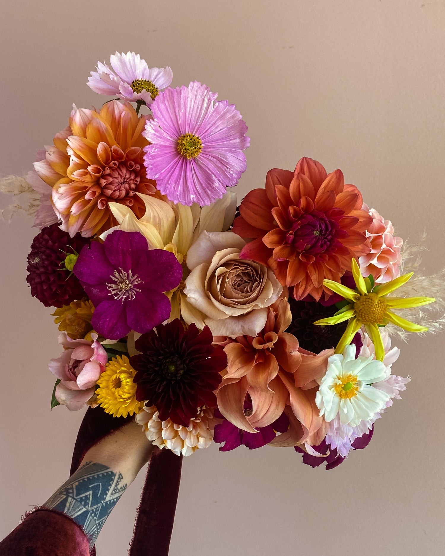 Bouquet of colorful flowers held by a person with tattoos on a neutral background