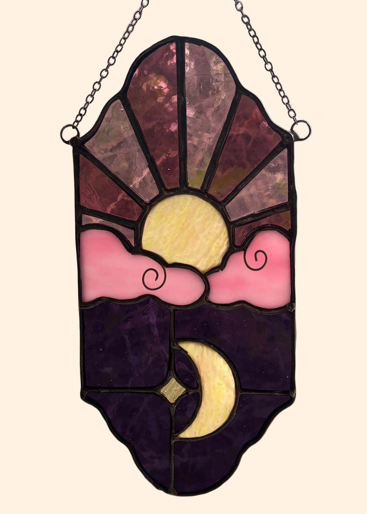 Stained glass panel with sun and moon design hanging indoors.