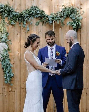 Wedding ceremony with a couple and officiant against a wooden backdrop with greenery