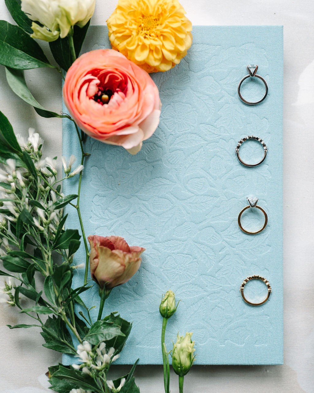 Three rings displayed on a textured blue card with flowers on a light background