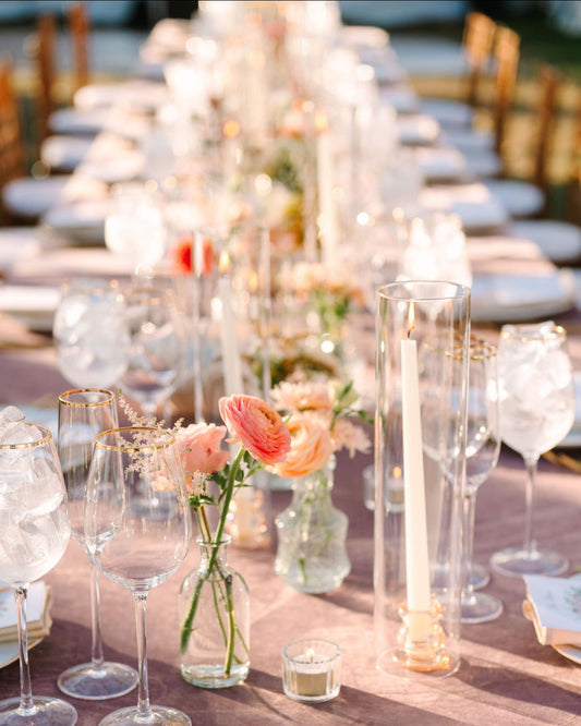 Decorative table setting with bud vases of flowers, glasses, and candles on a wooden table.