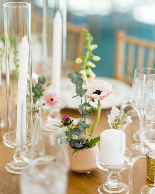 Table setting with floral centerpieces, candles, and glasses on a wooden table.