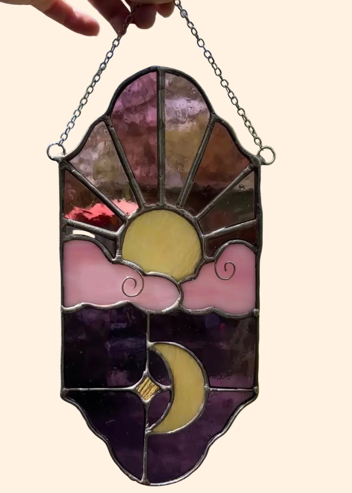 Stained glass panel with sun and moon design held in front of a blurred natural background