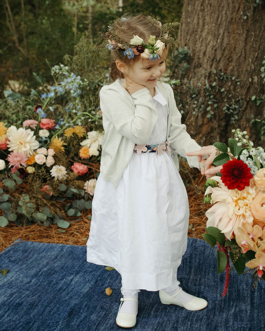 Two children in formal attire standing in a garden with floral decorations.