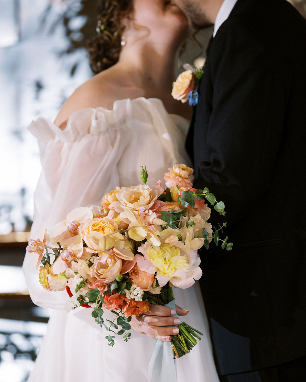 Couple in wedding attire with a colorful bouquet outdoors