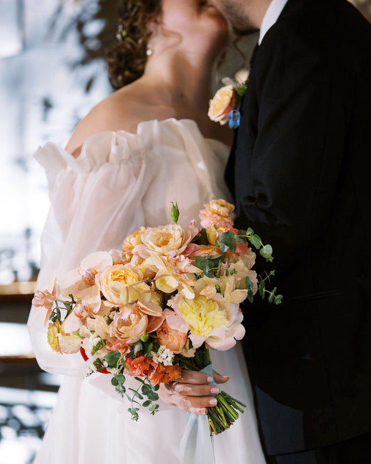 Couple in wedding attire with a colorful bouquet outdoors